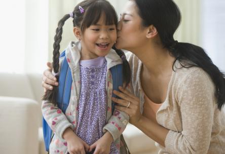 Mom kissing her daughter before sending her off to school.