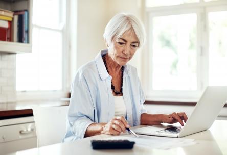 Older woman working at a laptop with a calculator.