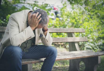 Photo: Man sitting on park bench with head in hands
