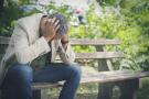 Photo: Man sitting on park bench with head in hands